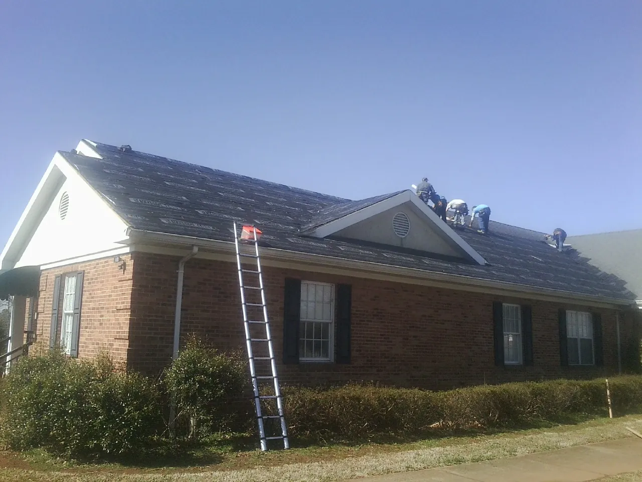 Crew tearing shingles off a brick ranch roof with a ladder set — Metal Roof Repair work by our crew in Cache Junction