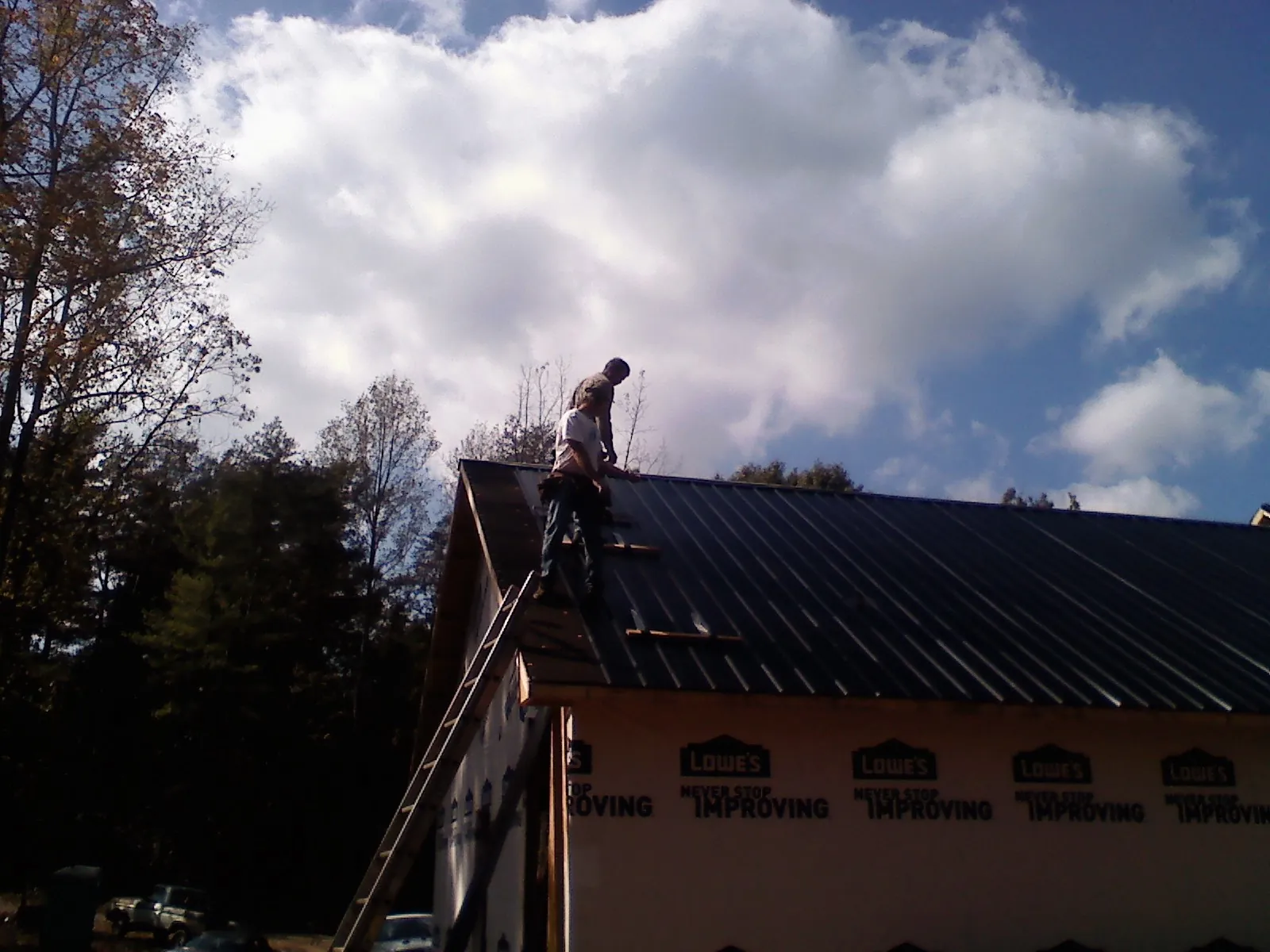 Roofer fastening dark metal panels high against a cloudy sky, from a Roof Inspection job in Cache Junction